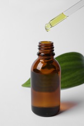 Photo of Dripping cosmetic oil from pipette into bottle on white background