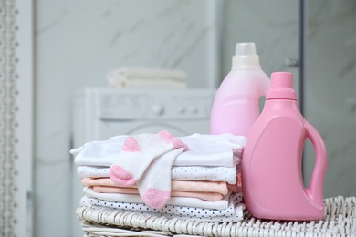 Photo of Bottles of detergent and children's clothes on wicker basket in bathroom