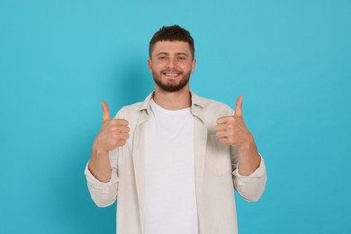 Photo of Young man showing thumbs up on light blue background