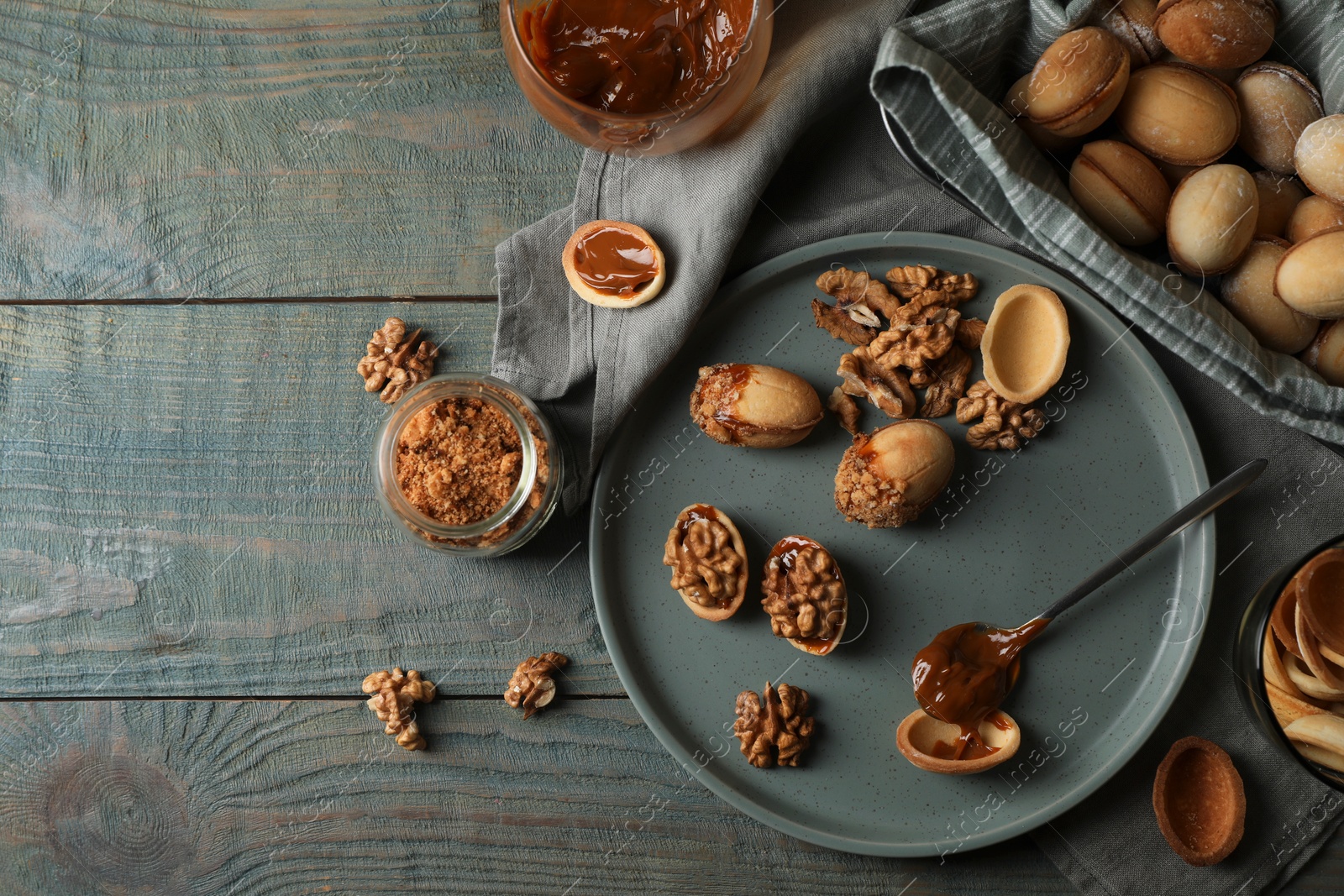 Photo of Freshly baked homemade walnut shaped cookies with nuts and boiled condensed milk on wooden table, flat lay. Space for text