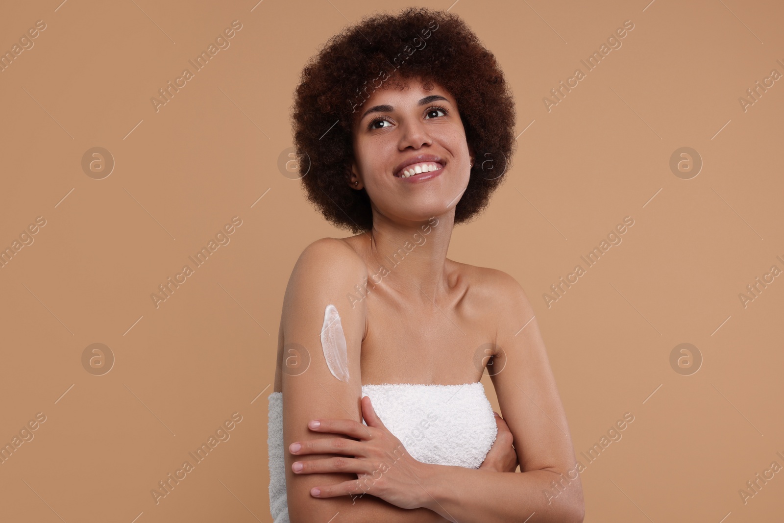 Photo of Beautiful young woman applying body cream onto arm on beige background