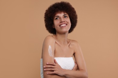 Photo of Beautiful young woman applying body cream onto arm on beige background