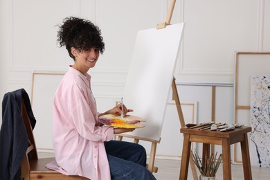 Young woman mixing paints on palette near easel in studio