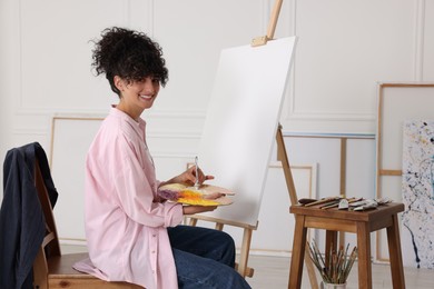 Photo of Young woman mixing paints on palette near easel in studio