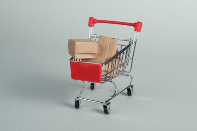 Photo of Small metal shopping cart with cardboard boxes on light background