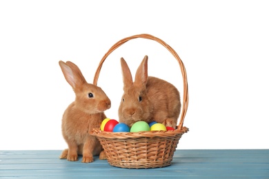 Photo of Cute fluffy bunnies and wicker basket with Easter eggs on light blue wooden table
