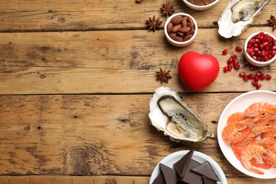 Photo of Natural aphrodisiac. Different food products and heart model on wooden table, flat lay. Space for text