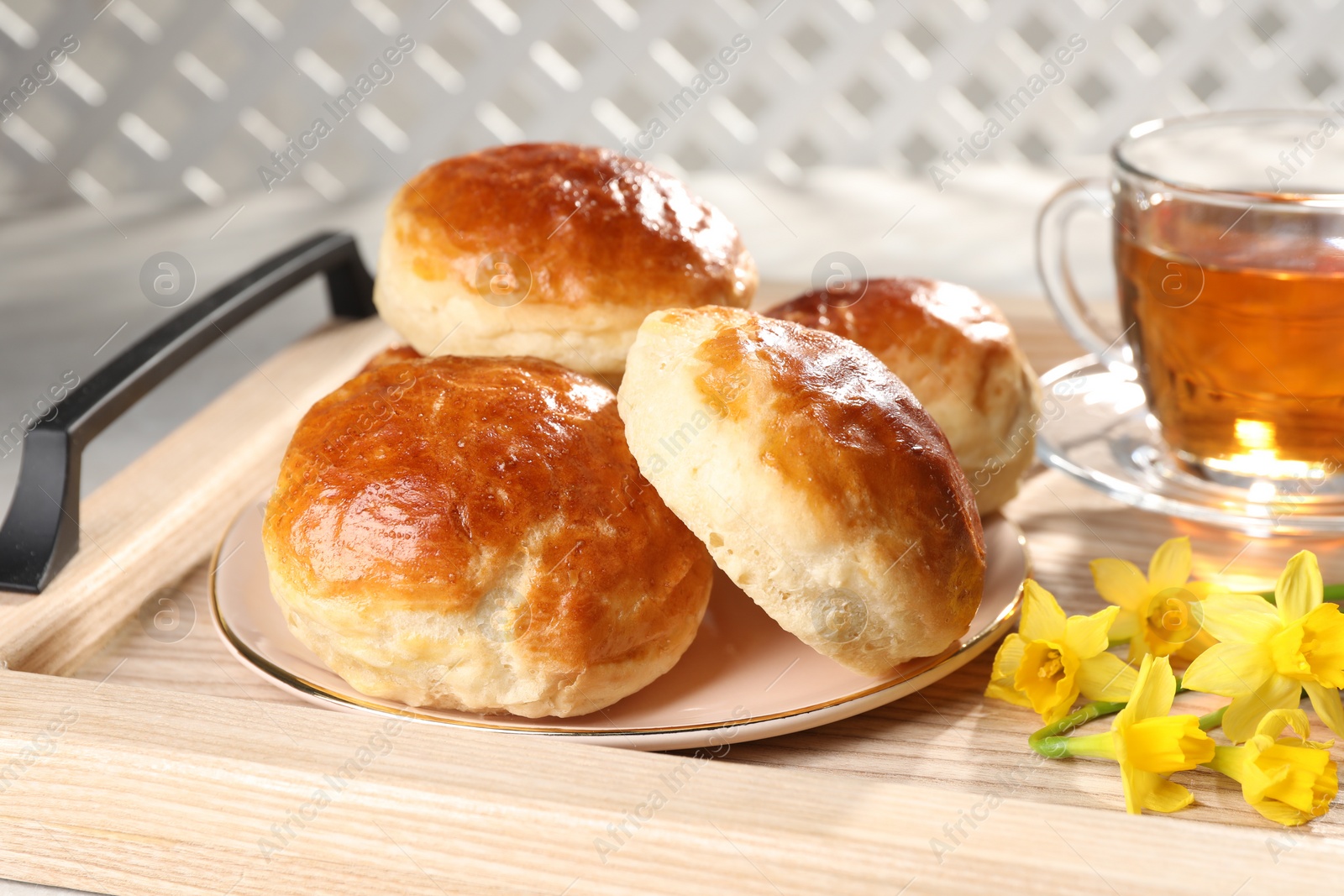 Photo of Freshly baked soda water scones, cup of tea and daffodils on wooden tray, closeup