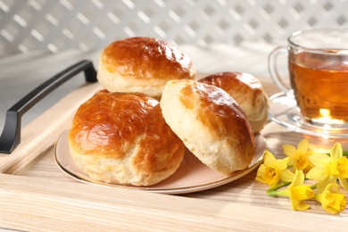 Photo of Freshly baked soda water scones, cup of tea and daffodils on wooden tray, closeup