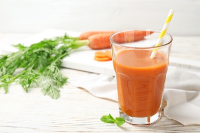 Glass of fresh carrot juice on white wooden table, space for text