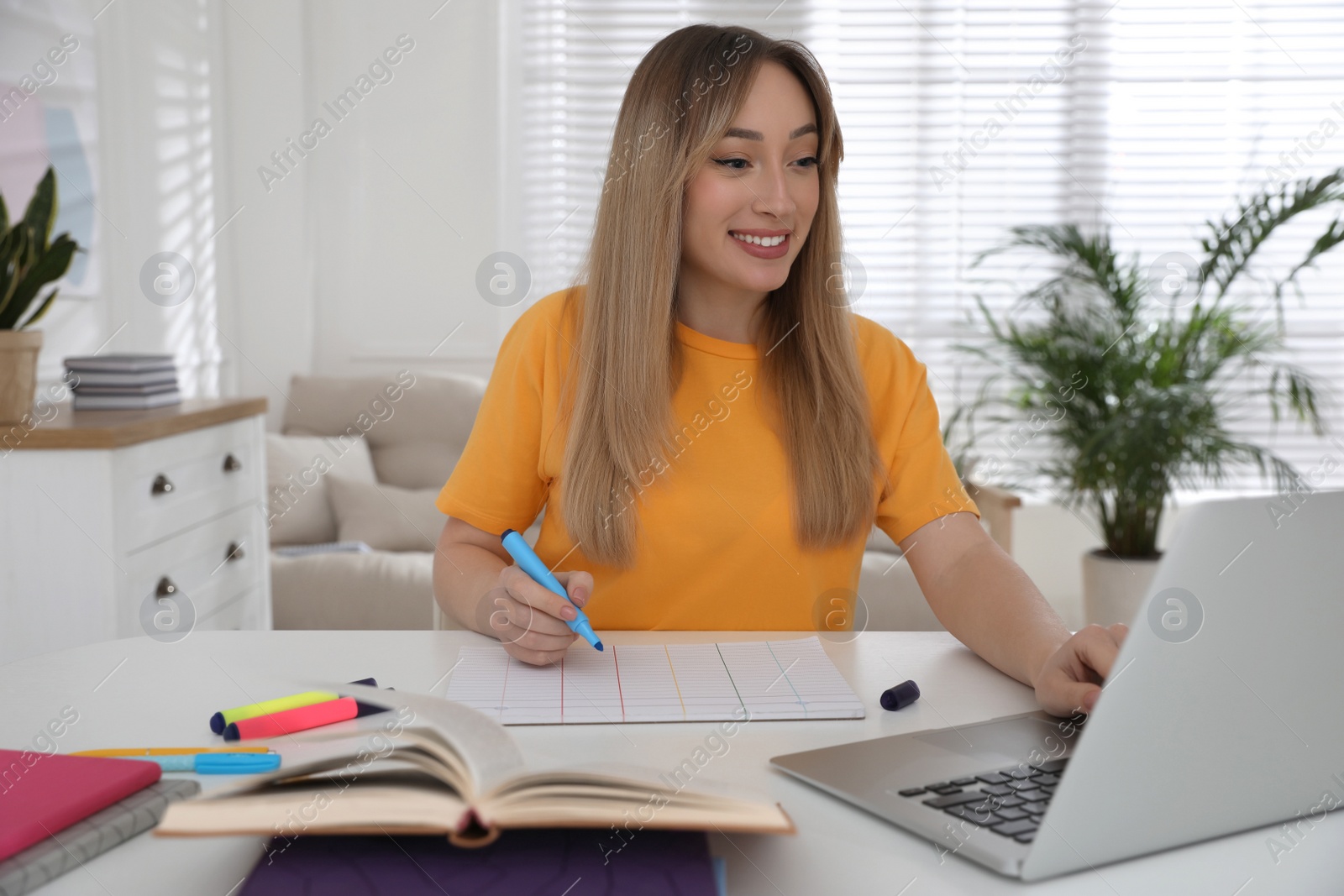 Photo of Young woman watching webinar at table in room