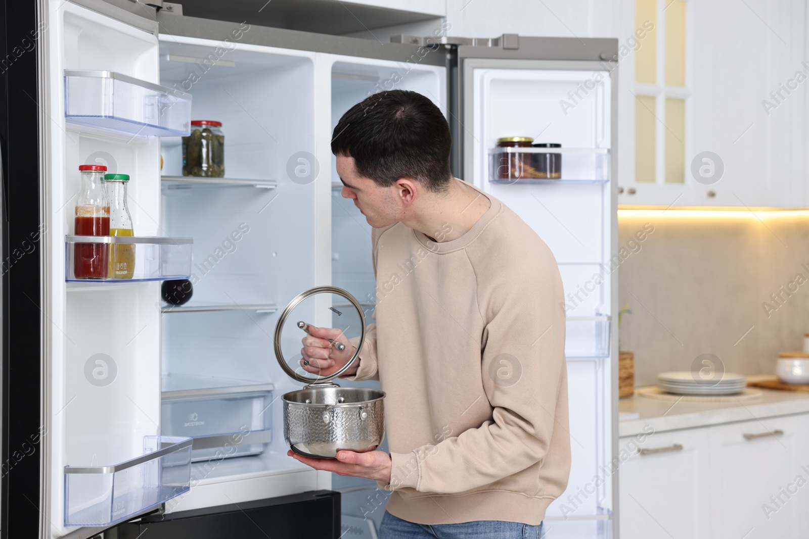 Photo of Man with pot near empty refrigerator in kitchen