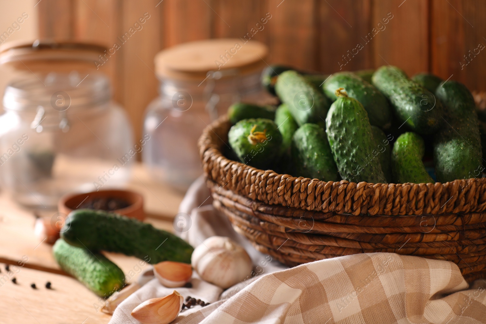 Photo of Fresh cucumbers and other ingredients near empty jars prepared for canning on wooden table, closeup