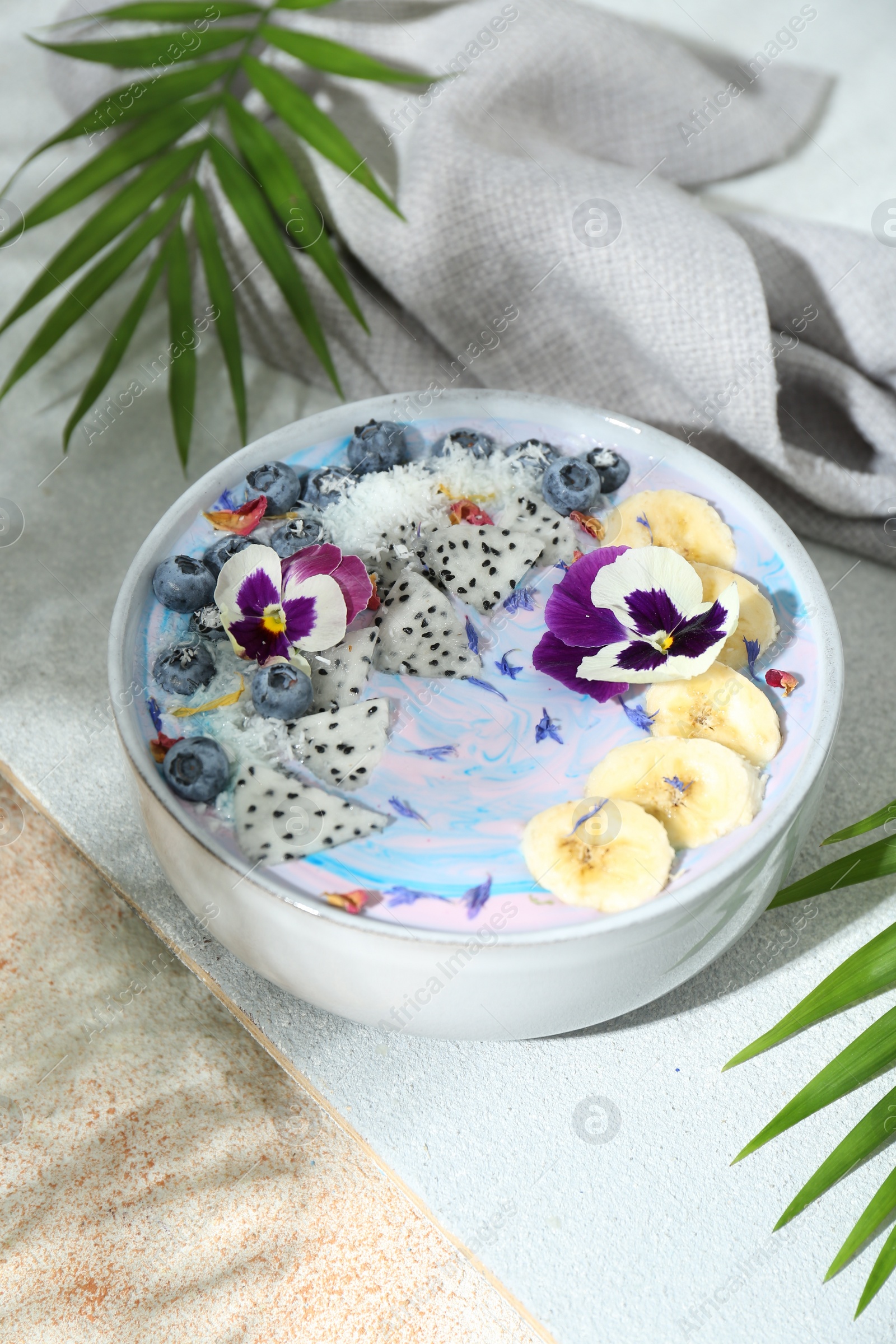 Photo of Delicious smoothie bowl with fresh fruits, blueberries and flowers on color textured table