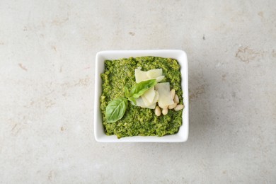 Bowl with delicious pesto sauce, cheese, pine nuts and basil leaves on light table, top view
