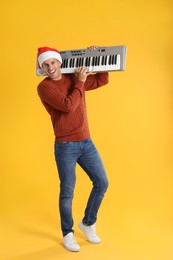 Man in Santa hat playing synthesizer on yellow background. Christmas music
