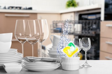 Image of Many clean tableware in kitchen. Dishwasher detergent falling into bowl with water