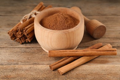 Photo of Aromatic cinnamon powder in mortar, sticks and pestle on wooden table