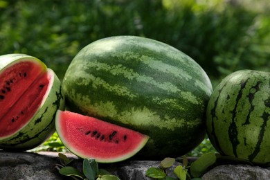 Photo of Different delicious ripe watermelons on stone surface outdoors, closeup