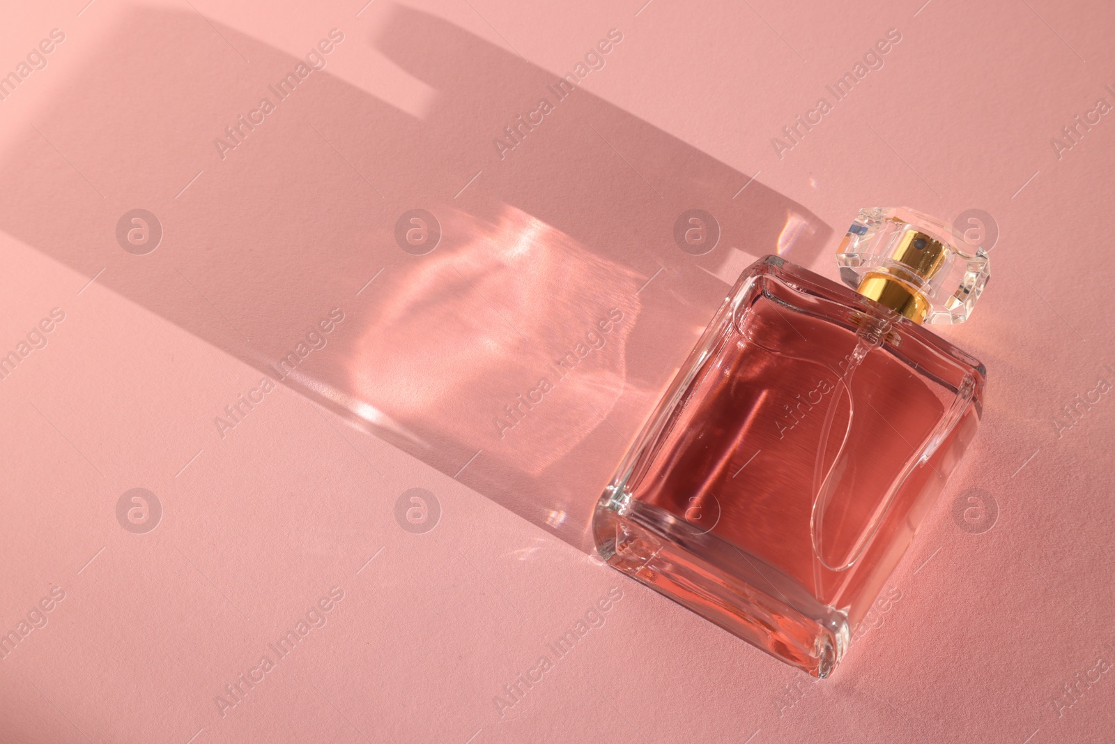 Photo of Luxury women's perfume. Sunlit glass bottle on pink background. Space for text