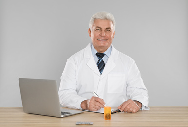 Professional pharmacist working at table against light grey background