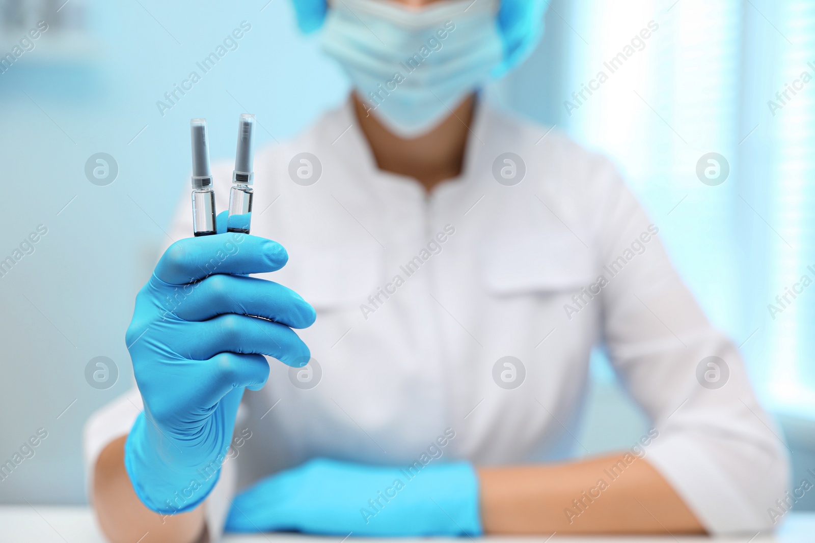 Photo of Doctor holding syringes with COVID-19 vaccine on blurred background, closeup