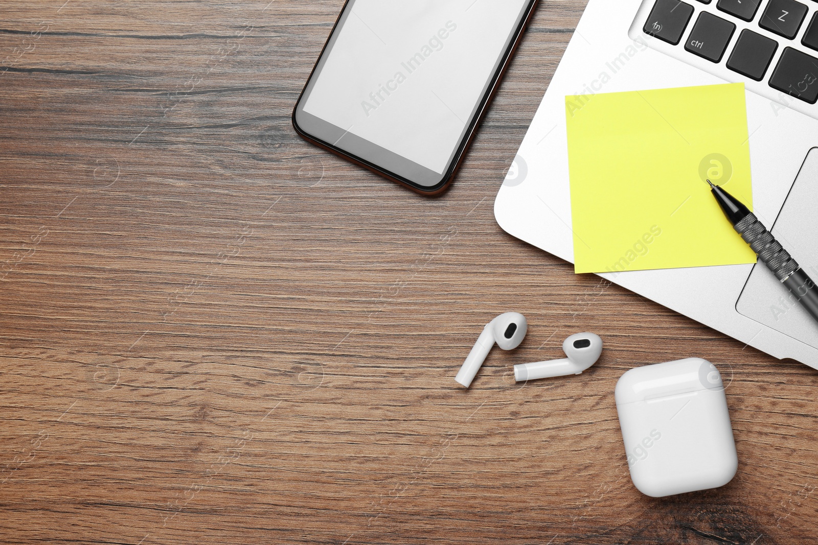 Photo of Laptop, smartphone, empty sticky note, pen and earphones on wooden table, flat lay. Space for text