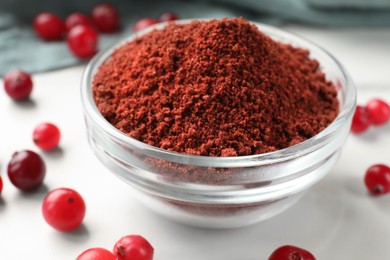 Photo of Dried cranberry powder in bowl and fresh berries on white table, closeup