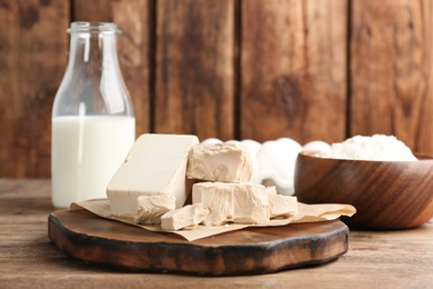 Photo of Pieces of compressed yeast near ingredients for dough on wooden table