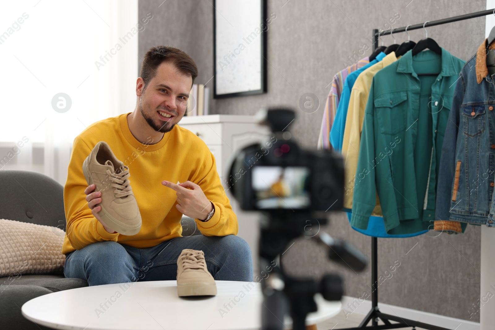 Photo of Smiling fashion blogger showing shoes while recording video at home