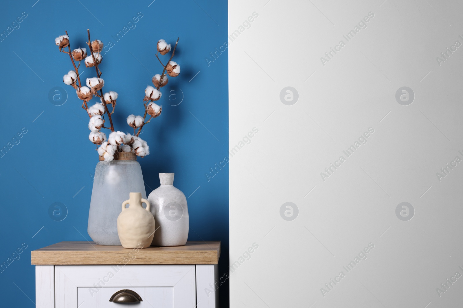 Photo of Vases and cotton branches on wooden table indoors. Space for text