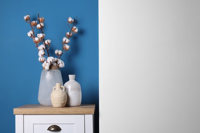 Vases and cotton branches on wooden table indoors. Space for text