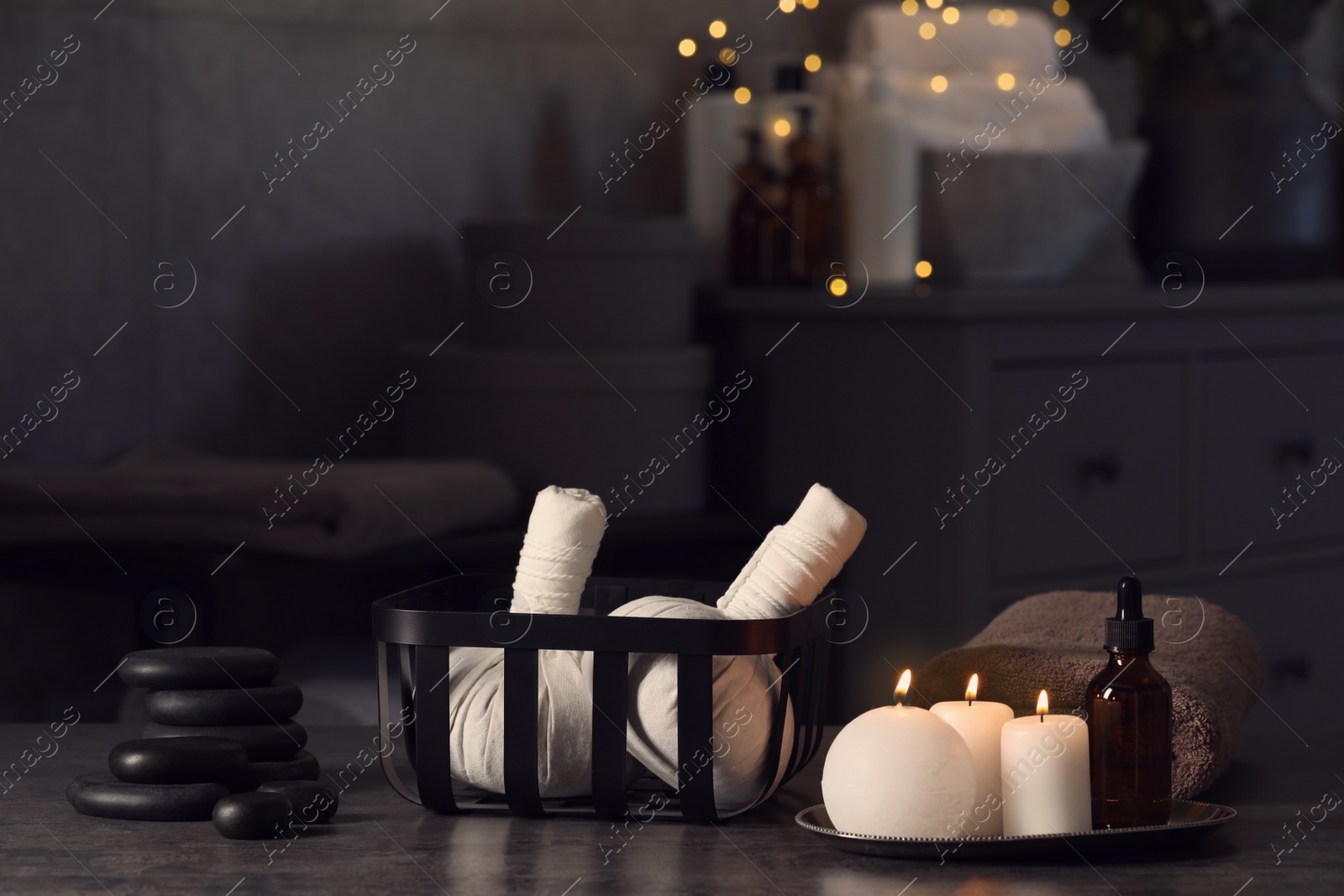 Photo of Herbal massage bags, burning candles and stones on grey table. Spa products