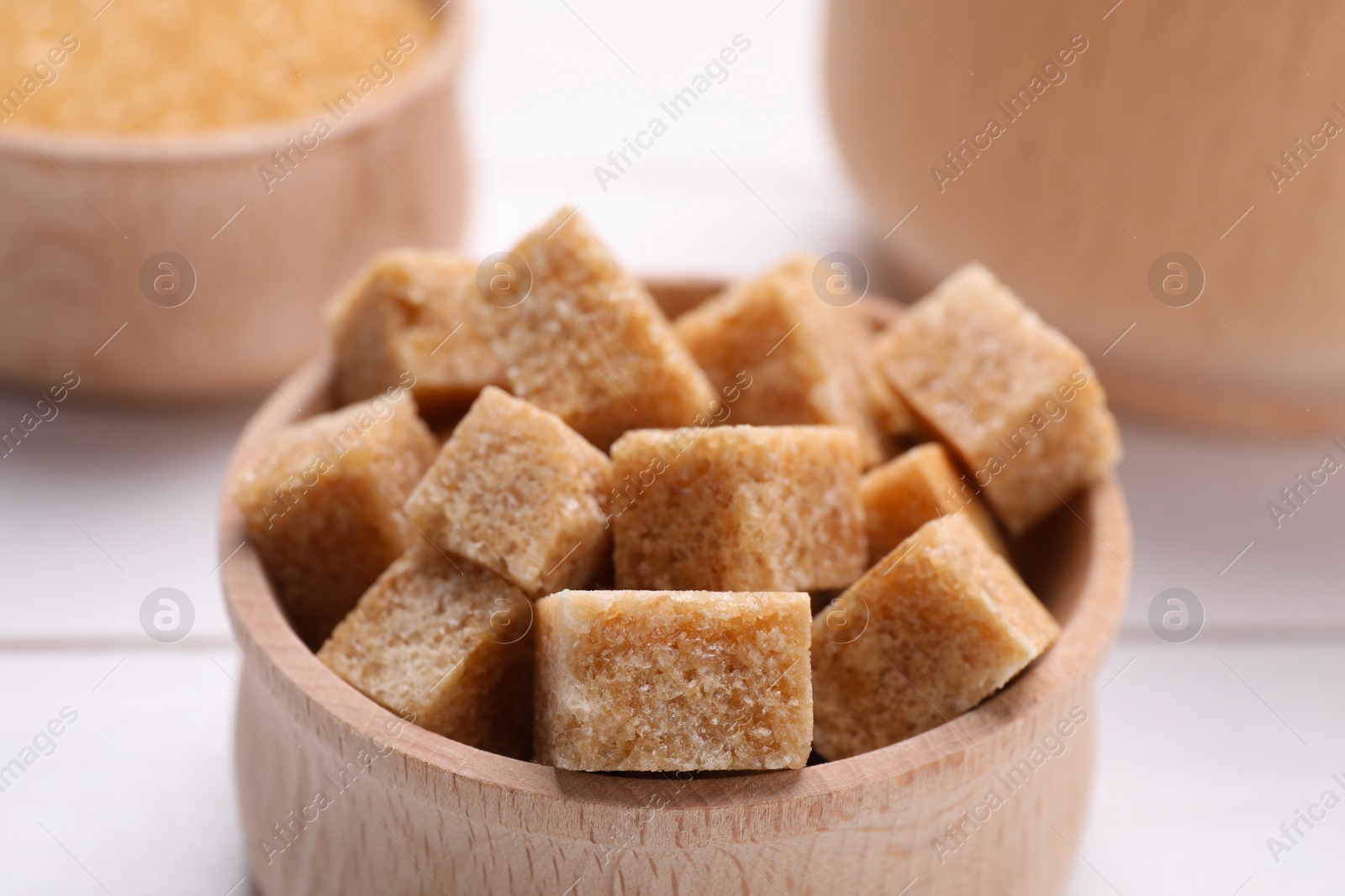 Photo of Brown sugar cubes in bowl on table, closeup