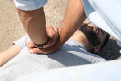 Passerby performing CPR on unconscious young man outdoors, closeup. First aid