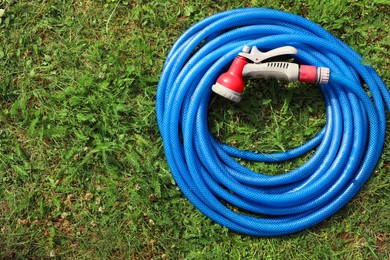 Photo of Watering hose with sprinkler on green grass outdoors, top view. Space for text