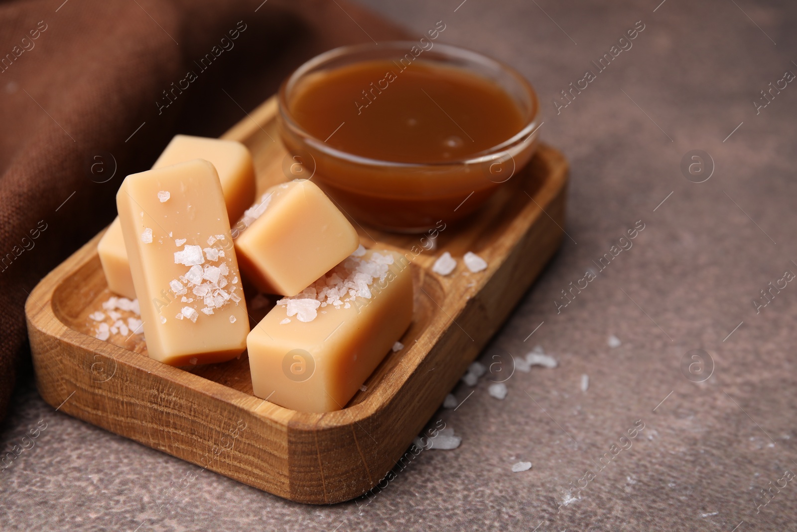 Photo of Yummy caramel candies, sauce and sea salt on brown table, closeup. Space for text