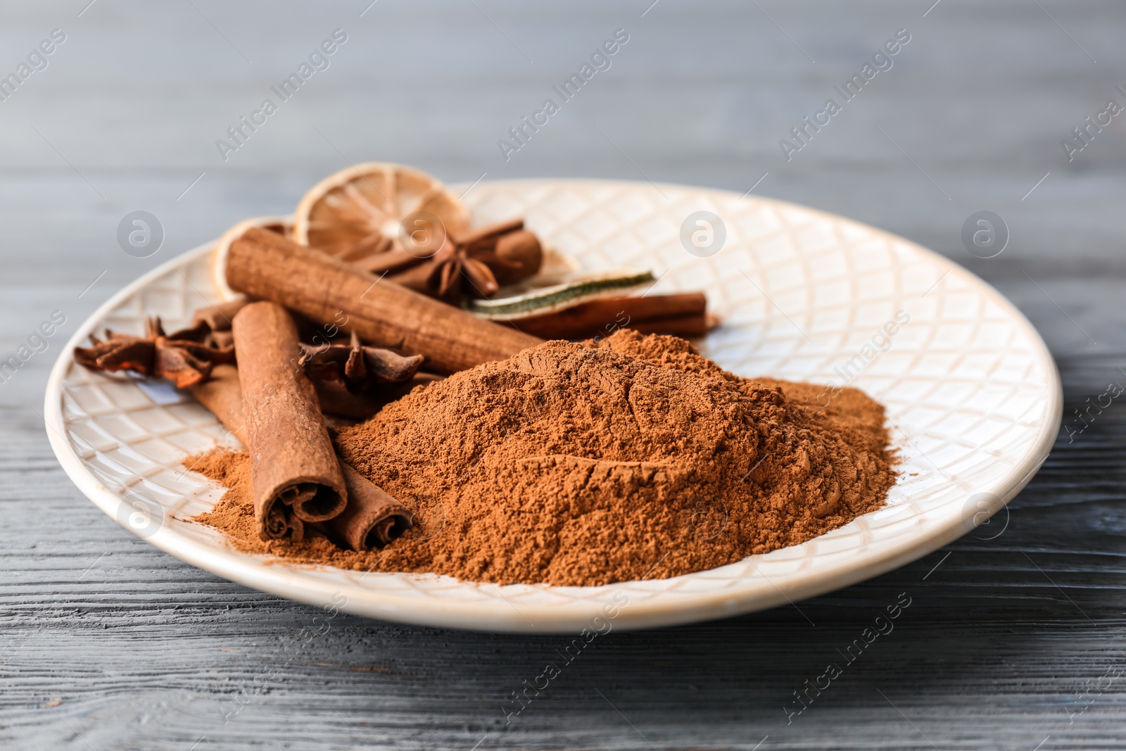 Photo of Plate with aromatic cinnamon sticks and powder on wooden background