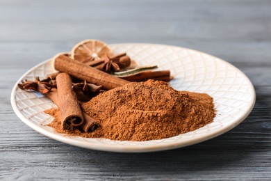 Plate with aromatic cinnamon sticks and powder on wooden background