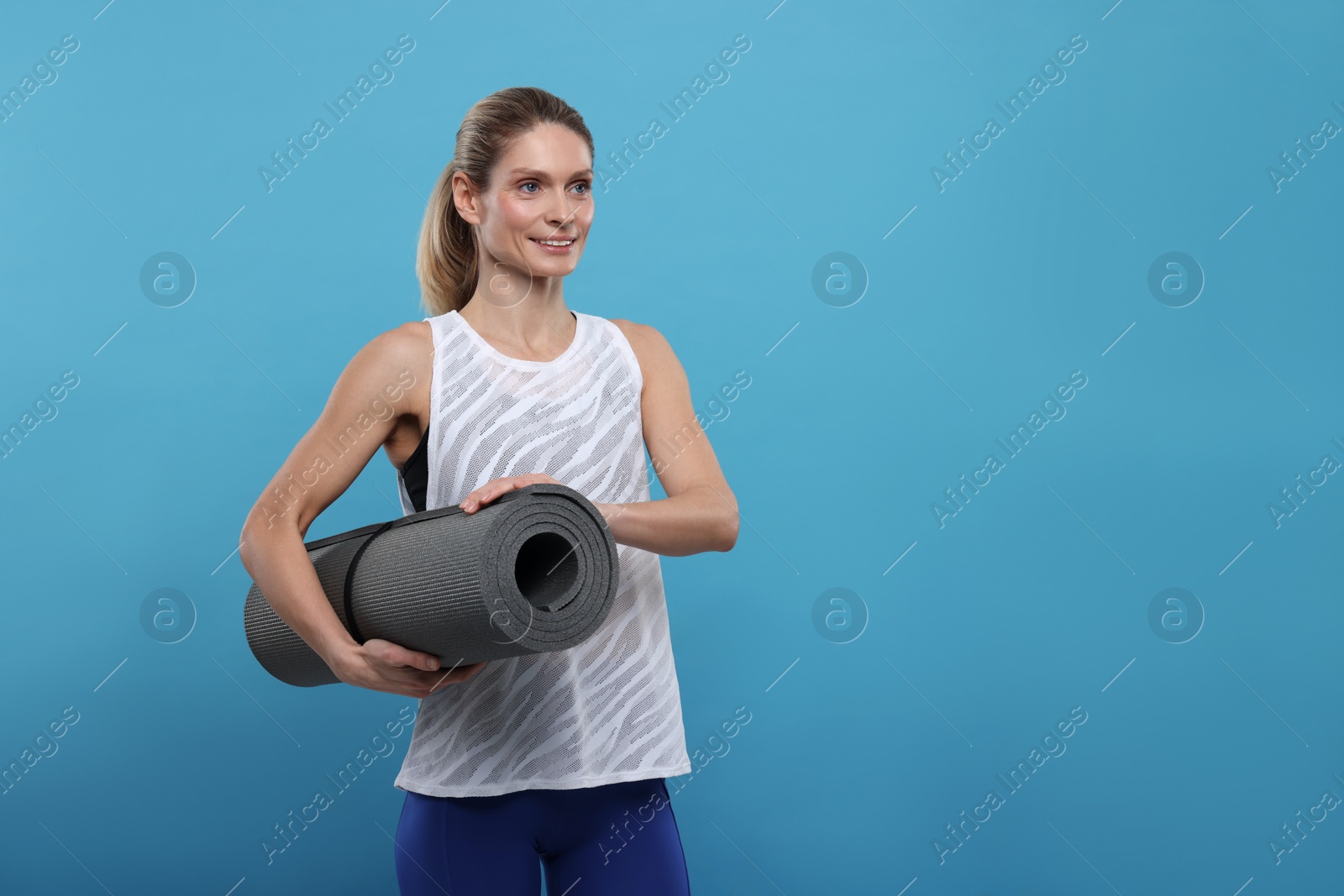 Photo of Sportswoman with fitness mat on light blue background, space for text