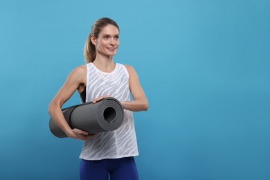 Photo of Sportswoman with fitness mat on light blue background, space for text