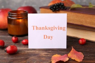 Paper card with words Thanksgiving Day near autumn leaves, berries, books and candle on wooden table, closeup