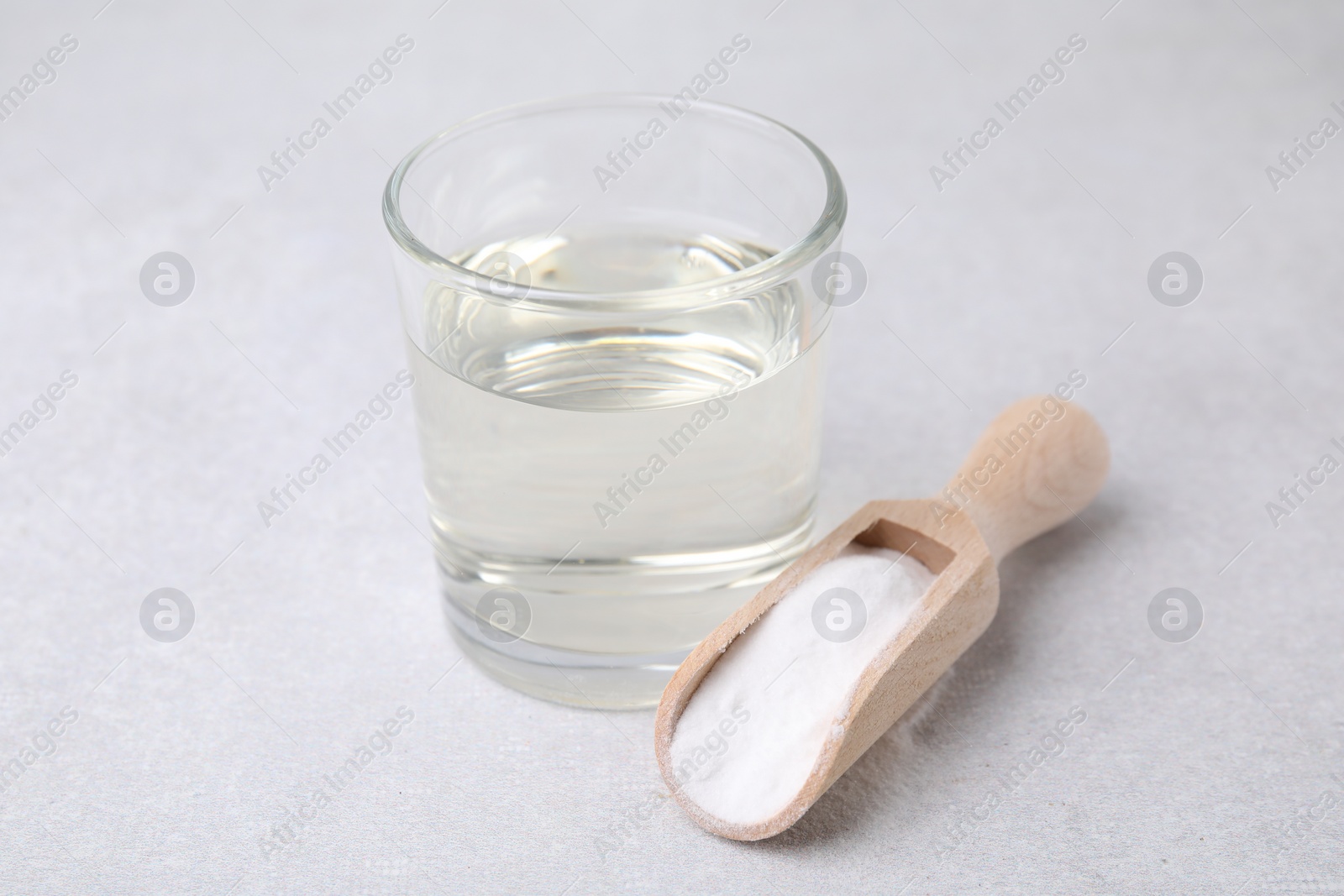 Photo of Vinegar in glass, baking soda and wooden scoop on light table