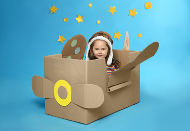 Photo of Little child playing with plane made of cardboard box near stars on blue background