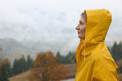 Photo of Young woman in raincoat enjoying mountain landscape under rain