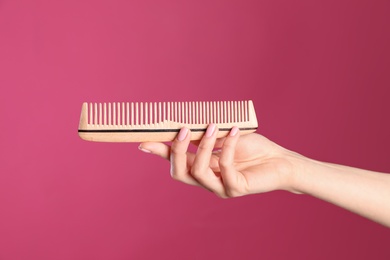 Photo of Woman holding wooden hair comb against crimson background, closeup