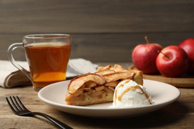 Slice of delicious apple pie served with ice cream and tea on wooden table