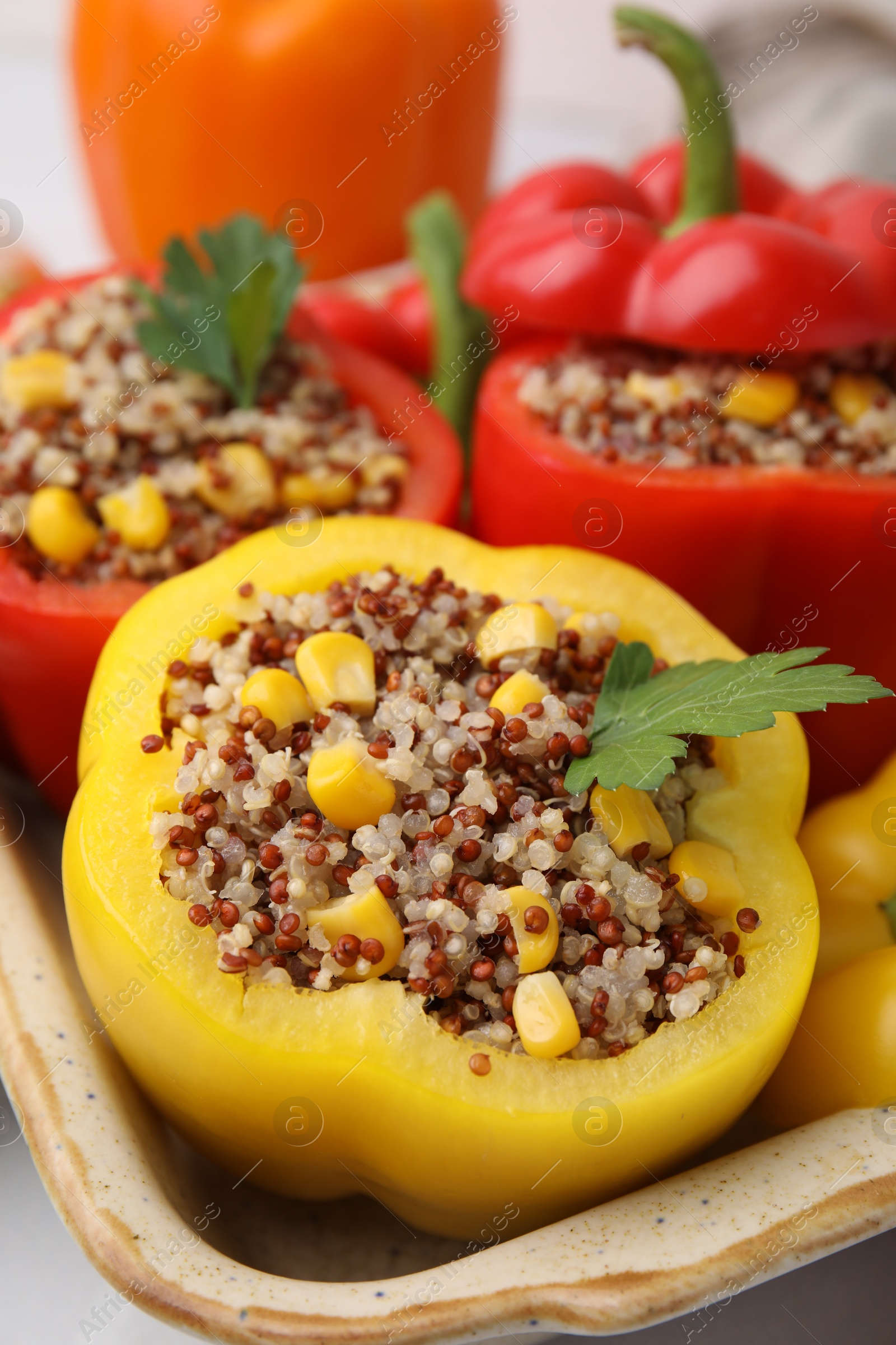 Photo of Quinoa stuffed bell peppers and parsley in baking dish on table, closeup