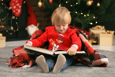 Little child reading book on floor at home. Christmas celebration