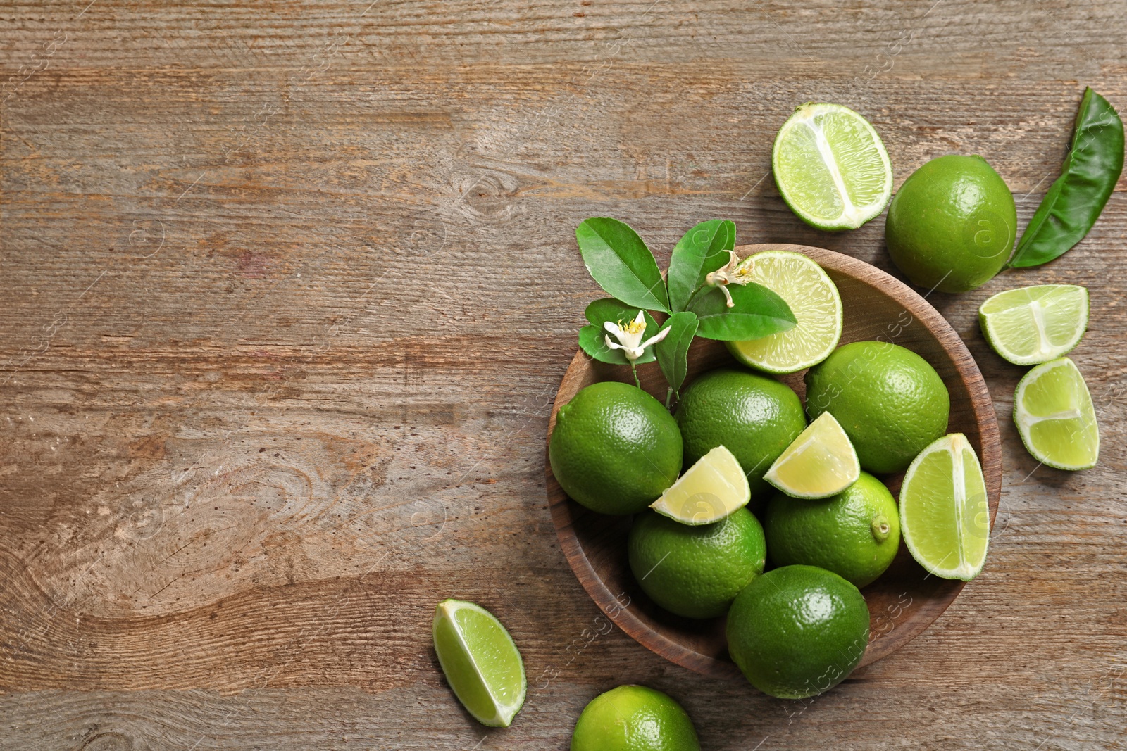 Photo of Bowl with fresh ripe limes on wooden background, top view